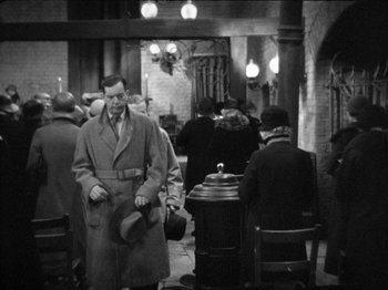 Movie still from “The Man Who Knew Too Much” (1934), directed by Alfred Hitchcock – An old photo of a man wearing a coat and hat; Medium shot, High angle