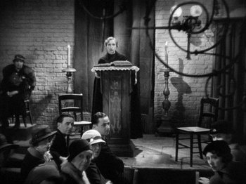 Movie still from “The Man Who Knew Too Much” (1934), directed by Alfred Hitchcock – An old photo of a man giving a lecture to a group; Wide shot, High angle