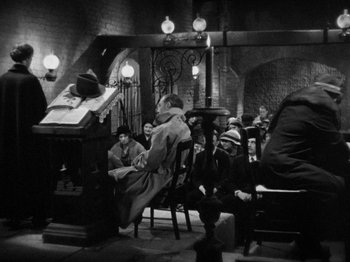 Movie still from “The Man Who Knew Too Much” (1934), directed by Alfred Hitchcock – A group of people sitting around a table; Wide shot, High angle