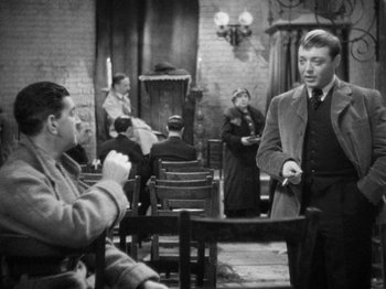 Movie still from “The Man Who Knew Too Much” (1934), directed by Alfred Hitchcock – A man in a suit and tie talking to another man in a suit and tie; Medium shot, Over the shoulder angle