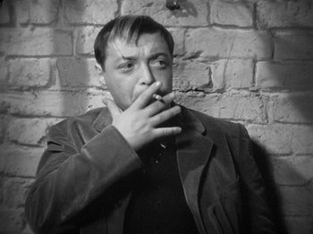 Movie still from “The Man Who Knew Too Much” (1934), directed by Alfred Hitchcock – A black and white photo of a man smoking a cigarette; Close Up shot, High angle