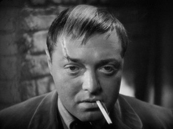 Movie still from “The Man Who Knew Too Much” (1934), directed by Alfred Hitchcock – A black and white photo of a man smoking a cigarette; Close Up shot, High angle