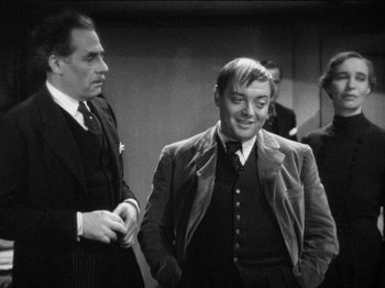 Movie still from “The Man Who Knew Too Much” (1934), directed by Alfred Hitchcock – A man in a suit standing next to another man in a suit; Medium shot, Over the shoulder angle