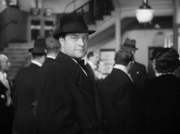 Movie still from “The Man Who Knew Too Much” (1934), directed by Alfred Hitchcock – Black and white photograph of a man wearing a hat; Medium shot, Low angle