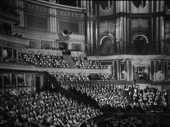 Movie still from “The Man Who Knew Too Much” (1934), directed by Alfred Hitchcock – An old photo of a large crowd of people in a large auditorium; Extreme Wide shot, High angle