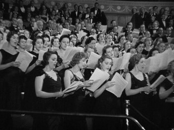 Movie still from “The Man Who Knew Too Much” (1934), directed by Alfred Hitchcock – A large group of people in black and white dresses; Medium shot, High angle