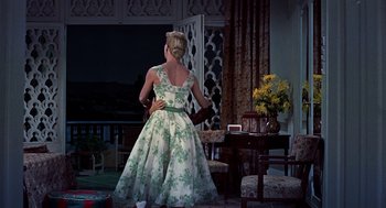 Movie still from “The Man Who Knew Too Much” (1956), directed by Alfred Hitchcock – A woman in a green and white dress standing in front of a chair; Wide shot, Low angle