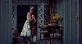 Movie still from “The Man Who Knew Too Much” (1956), directed by Alfred Hitchcock – A woman and a young boy hugging in front of a dining room table; Medium shot, Low angle