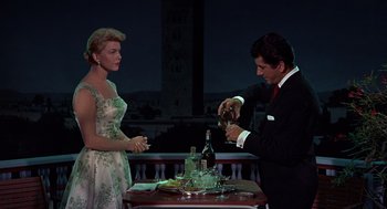 Movie still from “The Man Who Knew Too Much” (1956), directed by Alfred Hitchcock – A man and a woman standing next to each other at a dinner table; Medium shot, Low angle