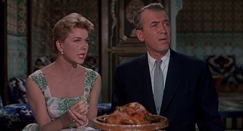 Movie still from “The Man Who Knew Too Much” (1956), directed by Alfred Hitchcock – An older man and a younger woman sitting in front of a turkey on a platter; Close Up shot, High angle
