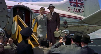 Movie still from “The Man Who Knew Too Much” (1956), directed by Alfred Hitchcock – A man and a woman are posing for a picture on a plane; Wide shot, Low angle