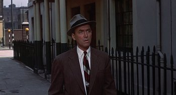 Movie still from “The Man Who Knew Too Much” (1956), directed by Alfred Hitchcock – A man in a suit and hat standing in front of a building; Medium shot, Low angle