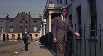 Movie still from “The Man Who Knew Too Much” (1956), directed by Alfred Hitchcock – A man in a suit and a hat walking down the street; Wide shot, Low angle
