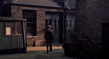 Movie still from “The Man Who Knew Too Much” (1956), directed by Alfred Hitchcock – A man in a suit and a hat is standing in front of a building; Wide shot, High angle