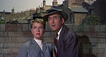 Movie still from “The Man Who Knew Too Much” (1956), directed by Alfred Hitchcock – A man and a woman standing next to each other in front of a brick wall; Close Up shot, Low angle