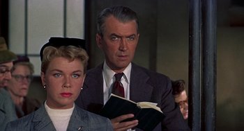 Movie still from “The Man Who Knew Too Much” (1956), directed by Alfred Hitchcock – A man in a suit and tie holding a book; Close Up shot, Low angle