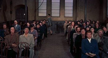 Movie still from “The Man Who Knew Too Much” (1956), directed by Alfred Hitchcock – A group of people sitting in a room with chairs; Wide shot, High angle