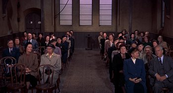 Movie still from “The Man Who Knew Too Much” (1956), directed by Alfred Hitchcock – A group of people standing in a room; Wide shot, High angle
