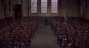 Movie still from “The Man Who Knew Too Much” (1956), directed by Alfred Hitchcock – An empty room filled with wooden chairs and tables; Wide shot, High angle