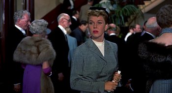 Movie still from “The Man Who Knew Too Much” (1956), directed by Alfred Hitchcock – A woman in a gray jacket holding a cigarette; Medium shot, Low angle