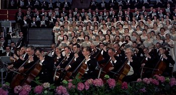 Movie still from “The Man Who Knew Too Much” (1956), directed by Alfred Hitchcock – A large group of people in formal wear holding musical instruments in front of an audience; Wide shot, High angle