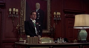 Movie still from “The Man Who Knew Too Much” (1956), directed by Alfred Hitchcock – A man sitting at a desk in front of a painting; Medium shot, Low angle