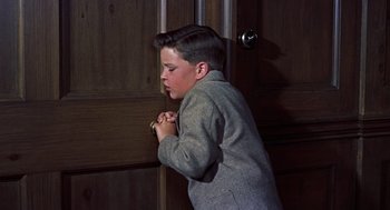 Movie still from “The Man Who Knew Too Much” (1956), directed by Alfred Hitchcock – A young boy standing in front of a wooden door; Medium shot, High angle