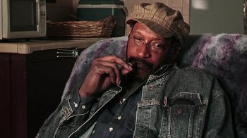 Movie still from “The Man from Earth” (2007), directed by Richard Schenkman – An older man sitting in a chair smoking a cigarette; Close Up shot, Low angle
