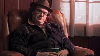 Movie still from “The Man from Earth” (2007), directed by Richard Schenkman – A man sitting in a chair holding a coffee cup; Medium shot, Over the shoulder angle