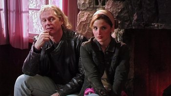 Movie still from “The Man from Earth” (2007), directed by Richard Schenkman – Two people sitting next to each other in front of a stone wall; Medium shot, Low angle