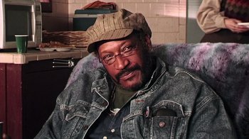 Movie still from “The Man from Earth” (2007), directed by Richard Schenkman – A man wearing a hat and glasses sitting in a chair; Close Up shot, Low angle