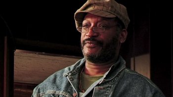 Movie still from “The Man from Earth” (2007), directed by Richard Schenkman – A person wearing glasses and a hat; Close Up shot, Low angle