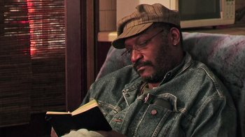 Movie still from “The Man from Earth” (2007), directed by Richard Schenkman – A man sitting in a chair reading a book; Close Up shot, High angle