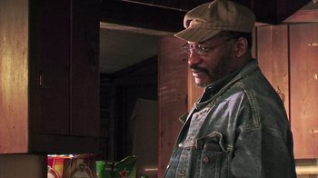 Movie still from “The Man from Earth” (2007), directed by Richard Schenkman – A man wearing a hat and glasses standing next to a window; Close Up shot, Over the shoulder angle