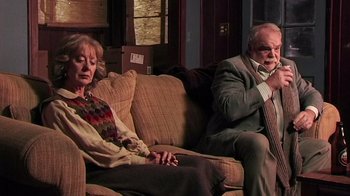 Movie still from “The Man from Earth” (2007), directed by Richard Schenkman – An older man and woman sitting on a couch next to each other; Medium shot, Over the shoulder angle