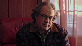 Movie still from “The Man from Earth” (2007), directed by Richard Schenkman – A man sitting in front of a wooden wall; Close Up shot, Over the shoulder angle