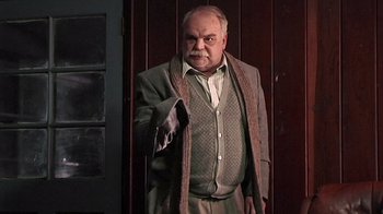 Movie still from “The Man from Earth” (2007), directed by Richard Schenkman – An older man in a suit and tie holding a gun; Medium shot, Low angle