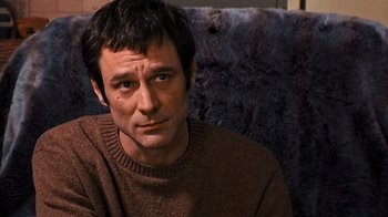 Movie still from “The Man from Earth” (2007), directed by Richard Schenkman – A person sitting on a couch wearing a sweater; Close Up shot, Low angle