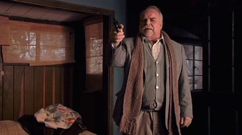 Movie still from “The Man from Earth” (2007), directed by Richard Schenkman – An older man holding a gun while wearing a scarf; Medium shot, Over the shoulder angle