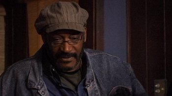 Movie still from “The Man from Earth” (2007), directed by Richard Schenkman – A man wearing a hat and glasses looking at the camera; Close Up shot, High angle