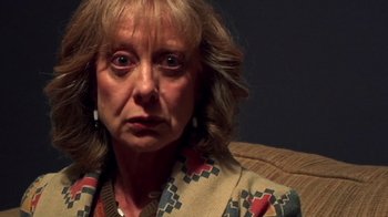 Movie still from “The Man from Earth” (2007), directed by Richard Schenkman – An older woman sitting on a couch looking at the camera; Close Up shot, Over the shoulder angle