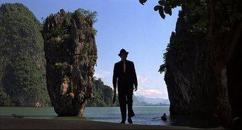 Movie still from “The Man with the Golden Gun” (1974), directed by Guy Hamilton – A man in a suit and a hat is walking by the water; Wide shot, Low angle