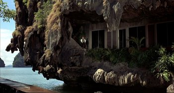 Movie still from “The Man with the Golden Gun” (1974), directed by Guy Hamilton – A man standing on a balcony of a house in the middle of a cliff; Extreme Wide shot, Low angle