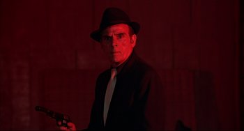 Movie still from “The Man with the Golden Gun” (1974), directed by Guy Hamilton – A man in a hat and a tie holding a gun; Medium shot, Low angle