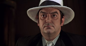 Movie still from “The Man with the Golden Gun” (1974), directed by Guy Hamilton – A person wearing a suit and a hat; Close Up shot, Low angle
