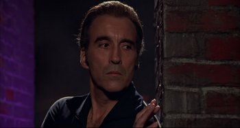 Movie still from “The Man with the Golden Gun” (1974), directed by Guy Hamilton – A person wearing a black shirt near a brick wall; Close Up shot, Low angle