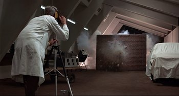 Movie still from “The Man with the Golden Gun” (1974), directed by Guy Hamilton – A man in a white lab coat is shooting a gun; Wide shot, Low angle