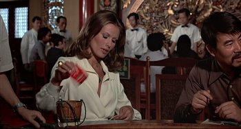 Movie still from “The Man with the Golden Gun” (1974), directed by Guy Hamilton – A woman sitting at a table in front of a drink; Medium shot, Over the shoulder angle