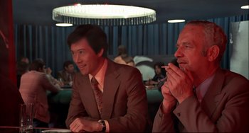 Movie still from “The Man with the Golden Gun” (1974), directed by Guy Hamilton – A couple of men sitting next to each other in a room; Medium shot, Low angle