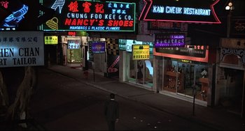 Movie still from “The Man with the Golden Gun” (1974), directed by Guy Hamilton – A man walking down the street at night in front of many stores; Extreme Wide shot, High angle